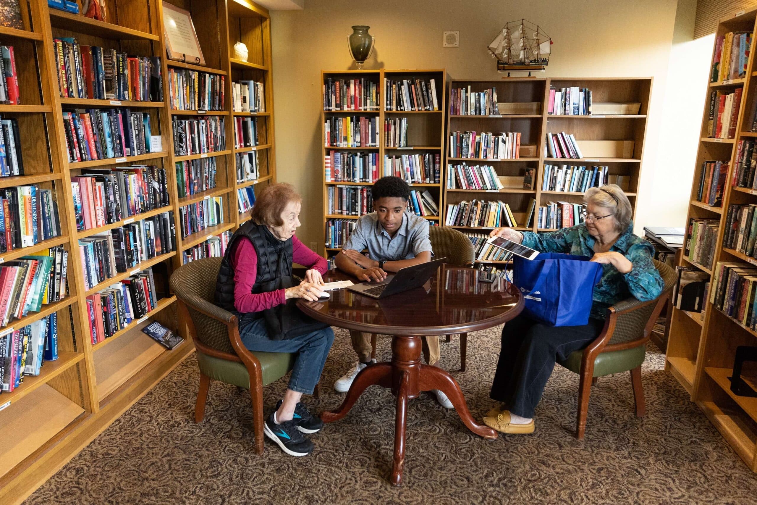 Graham Bennett, 14, teaches Jane Katz, left, how to use her laptop as Birgit Andersen, right, awaits her turn. Bennet is a tech wizard who comes to The Kenwood Retirement Community once a week to help residents with their phones, iPads, laptops, and computers.